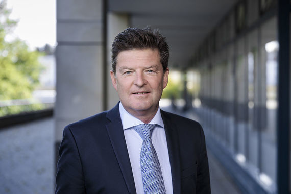 Ein Mann im Anzug und Krawatte steht im Freien vor einem Gebäude.