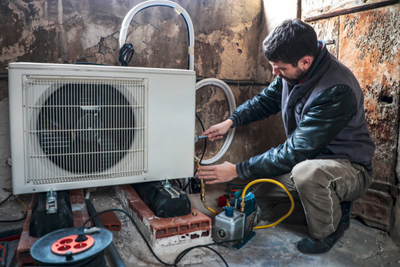 Ein Techniker arbeitet an einem Außenblock eines Klimageräts in einem rustikalen Raum.