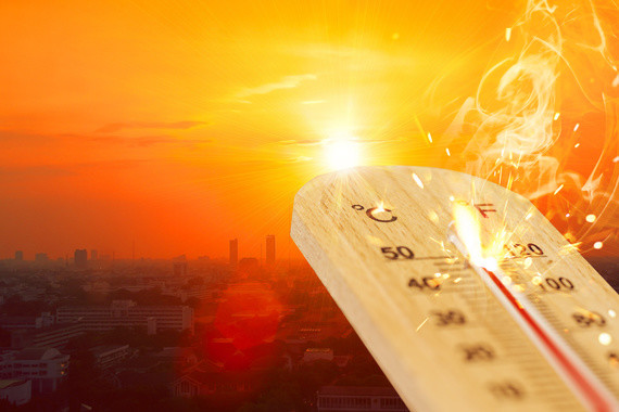 Ein Thermometer zeigt hohe Temperaturen an, vor einem Hintergrund eines leuchtenden Sonnenuntergangs über einer Stadt.