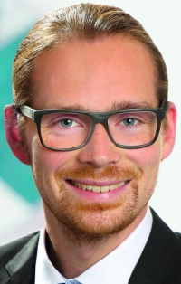 Ein Mann mit Brille, Bart und blonden Haaren lächelt in die Kamera.