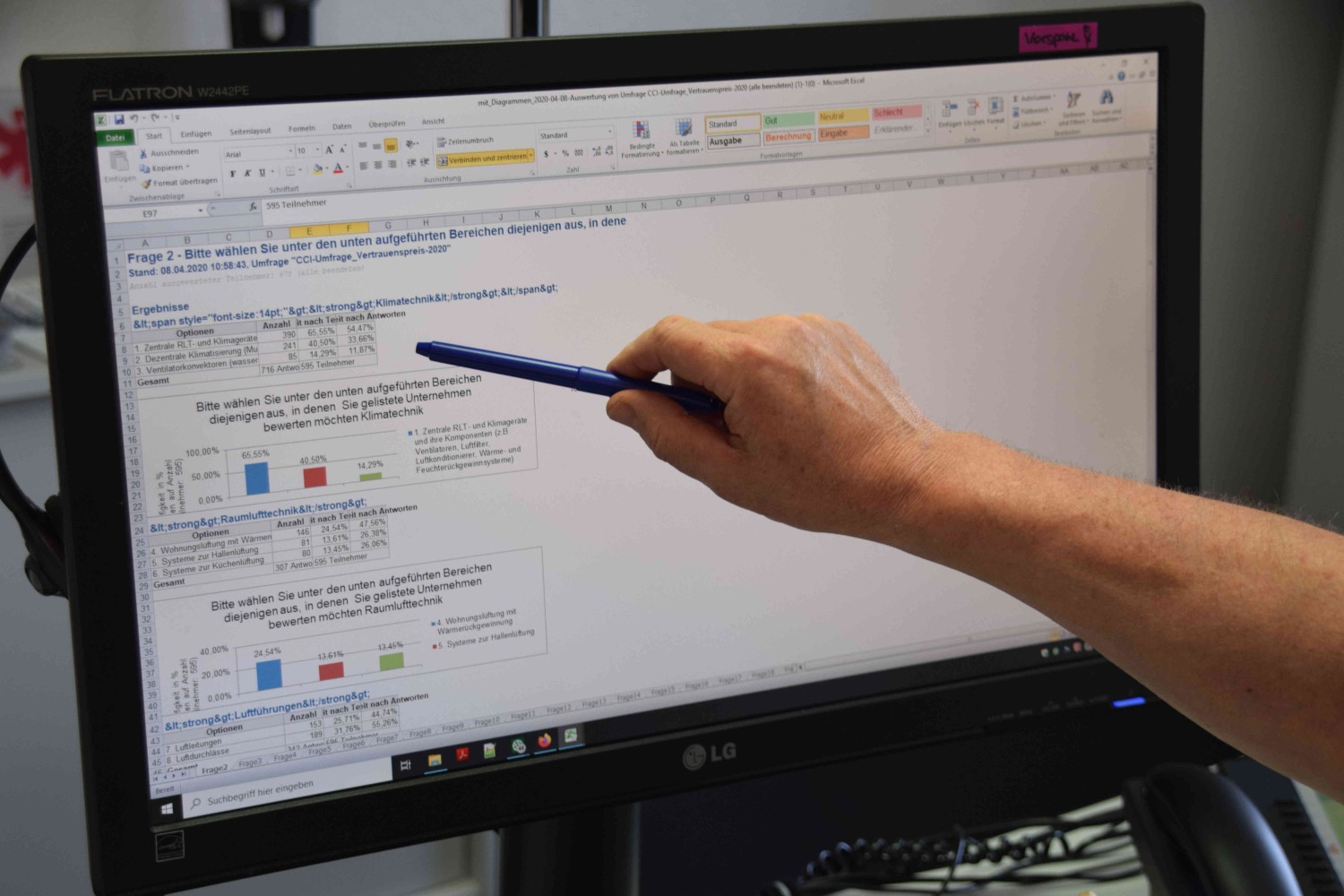 Eine Hand mit einem Stift zeigt auf einen Computerbildschirm, auf dem ein Dokument mit Text und farbigen Balken angezeigt wird.