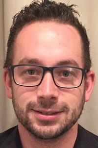 Ein Mann mit kurzen dunklen Haaren, Brille und Bart trägt ein dunkles Hemd.