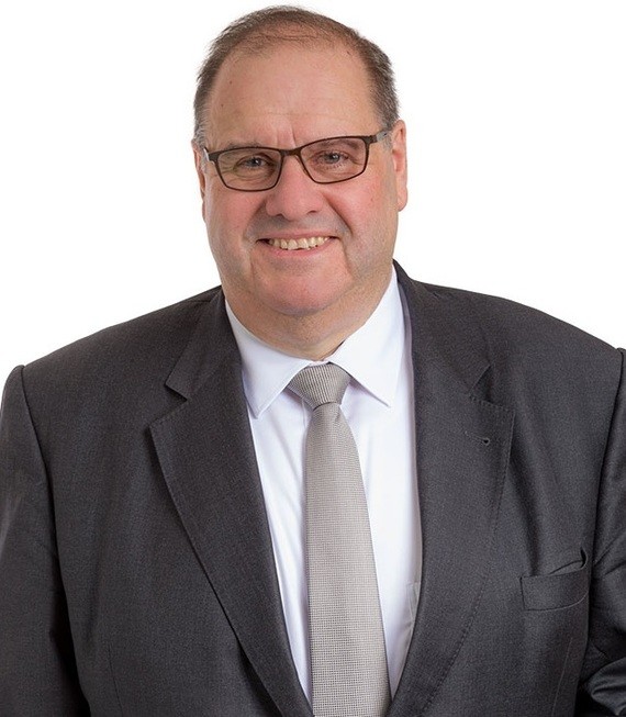 Ein Mann im Anzug und mit Brille lächelt in die Kamera.