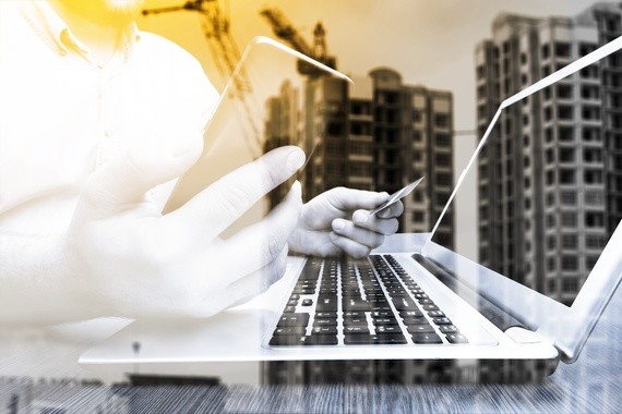 Eine Person tippt auf einer Laptop-Tastatur, während im Hintergrund ein Baustellenhintergrund mit Wolkenkratzern zu sehen ist.