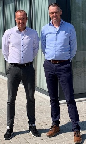 Zwei Männer stehen nebeneinander auf einem Gehweg vor einem Gebäude.