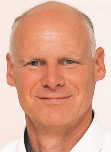 Ein Mann mit kahlen Haaren und einem Lächeln trägt ein weißes Hemd.