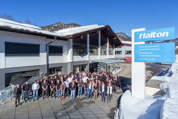 Gruppe von Menschen steht vor einem modernen Gebäude mit dem Logo 