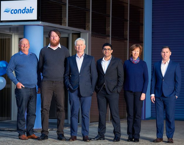 Sechs Personen stehen nebeneinander vor einem Gebäude mit dem Logo von 