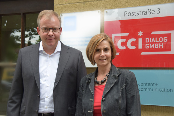 Zwei Personen stehen vor einem Firmenschild mit der Aufschrift 