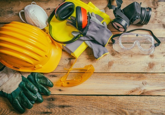 Arbeits- und Sicherheitsausrüstung, darunter Helm, Handschuhe, Schutzbrille und Schutzhelm, auf einem Holztisch.