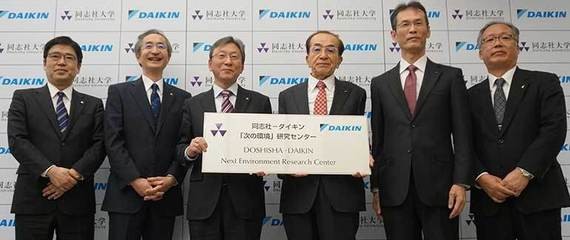 Fünf Männer in Anzügen stehen nebeneinander und halten eine große Urkunde, wobei im Hintergrund das Logo von Mitsubishi zu sehen ist.