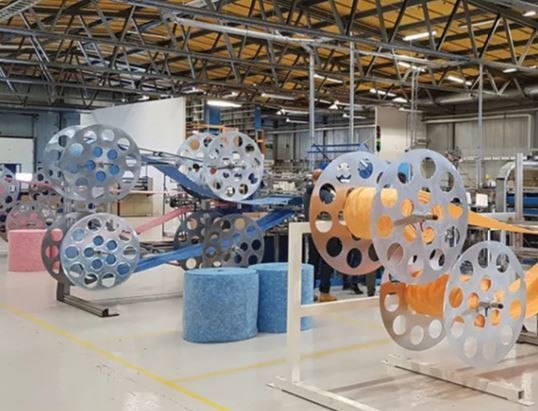 Eine industrielle Produktionsanlage mit großen, farbigen Walzen und Förderbändern in einem hell erleuchteten Werkshof.