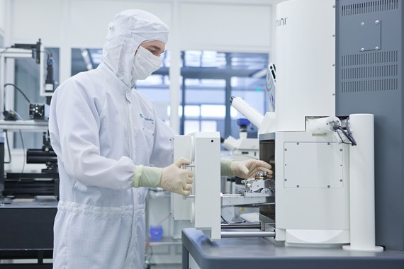 Eine Person in Schutzkleidung bedient eine Labormaschine in einer sauberen Arbeitsumgebung.