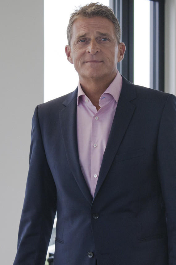 Ein Mann im Anzug mit rosa Hemd steht vor einem Fenster.