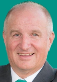 Ein Mann mit grauem Haar und Bart lächelt vor einem grünen Hintergrund.