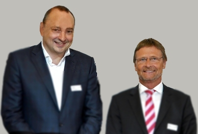 Zwei Männer in Anzügen stehen nebeneinander, beide lächeln und tragen Namensschilder.