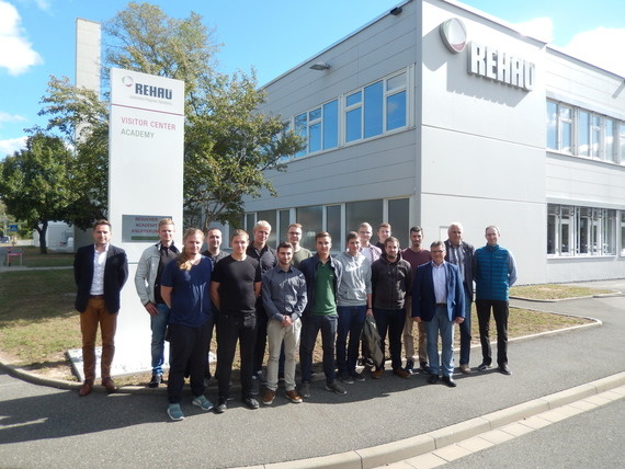 Gruppe von Menschen steht vor einem modernen Gebäude mit dem Logo 