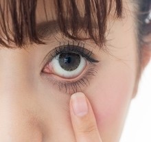 Eine Nahaufnahme einer Person, die mit dem Finger sanft auf ihre Wimpern zeigt.