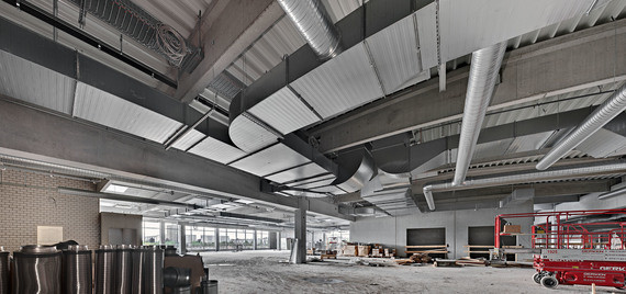 Innenansicht eines industriellen Raums mit offenem Dach, Rohrleitungen und Werkzeugen im Hintergrund.