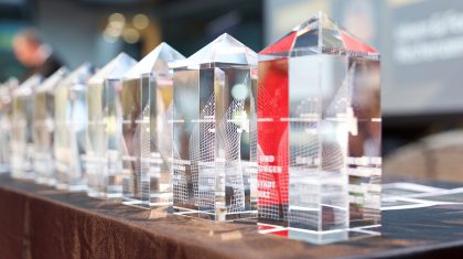 Eine Reihe von transparenten Kristallpreisstatuen mit roten Akzenten steht auf einem Tisch.