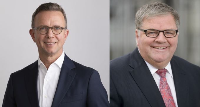 Zwei Männer in Anzügen und Krawatten lächeln in die Kamera.