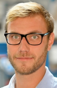 Ein Mann mit blonden Haaren, Brille und Bart trägt ein hellblaues Hemd.