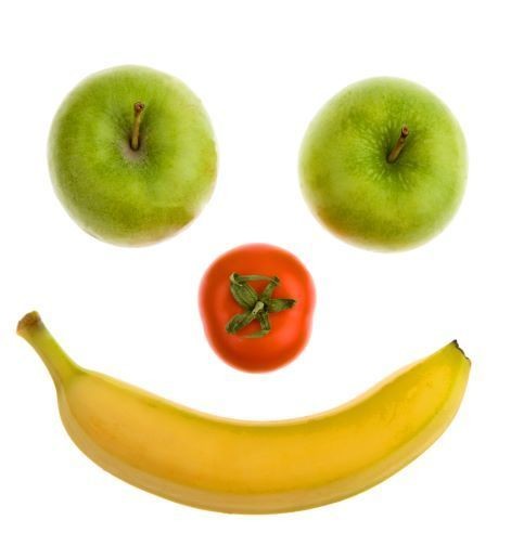 Ein Bild von einem Lächeln, das aus zwei grünen Äpfeln als Augen, einem roten Tomaten als Mund und einer gelben Banane als Mundwinkel besteht.