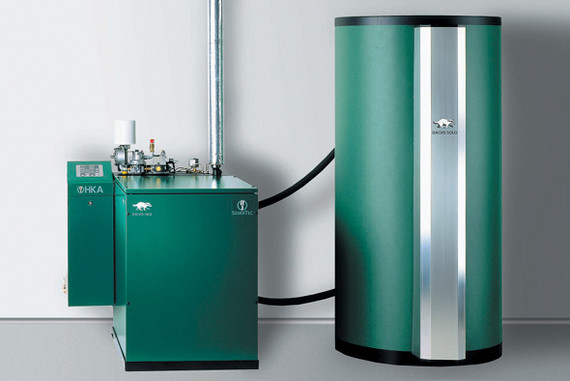 Zwei grüne Heizungsgeräte, darunter ein Boiler und ein kleinerer Kasten, stehen nebeneinander in einem technischen Raum.