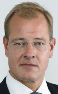 Ein Mann mit blondem Haar und blauem Hemd schaut direkt in die Kamera.