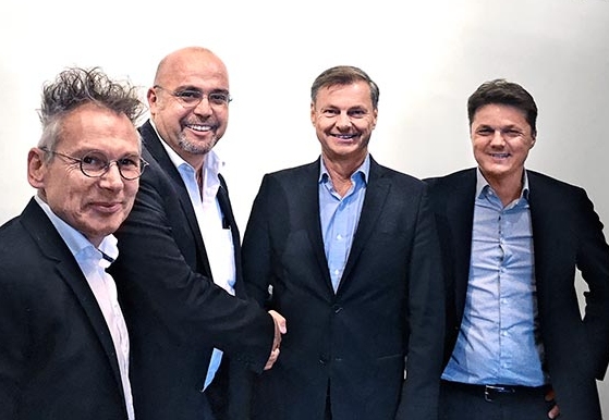 Vier Männer in Anzügen stehen nebeneinander und schütteln Hände.