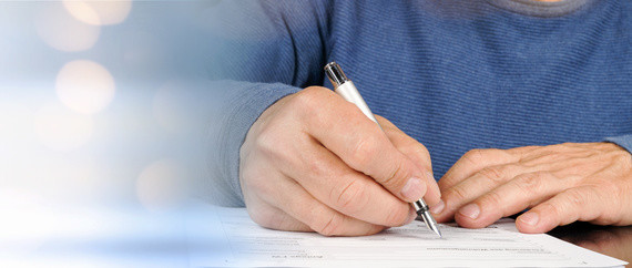 Eine Person schreibt mit einem Stift auf ein Blatt Papier.