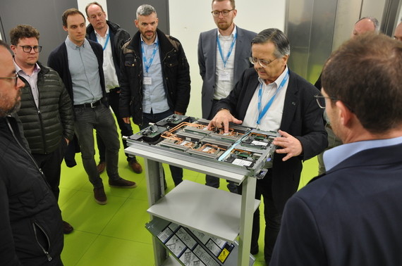 Eine Gruppe von Menschen steht um einen Tisch mit elektronischen Geräten und diskutiert.