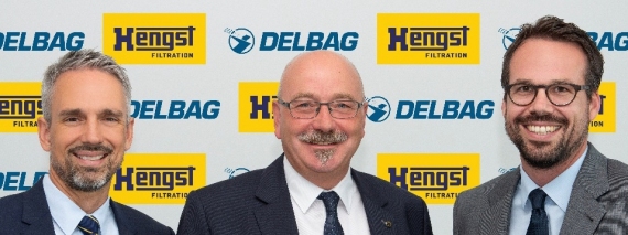 Drei Männer in Anzügen stehen nebeneinander vor Logos von 