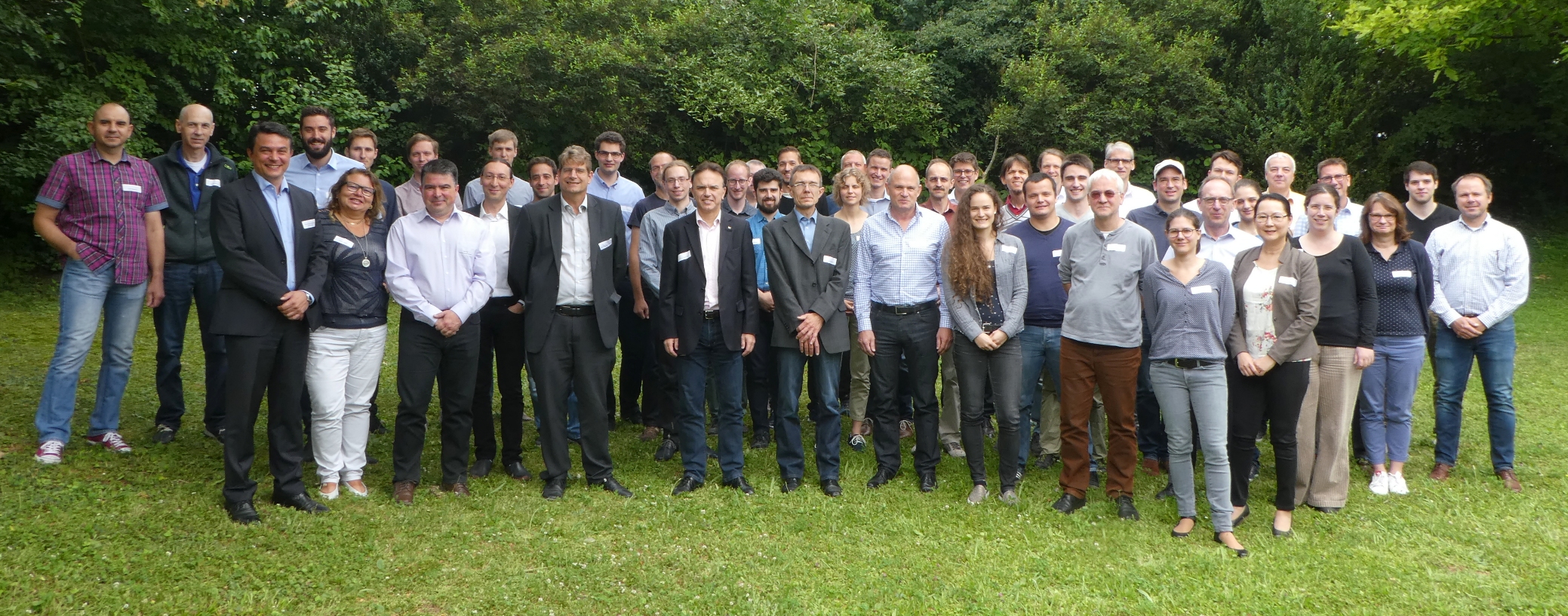 Gruppe von Menschen steht im Freien auf einem Rasen, lächelnd und nebeneinander gestanden.