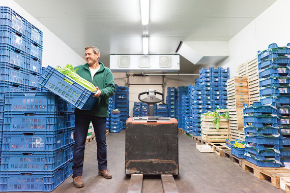 Eine Person steht in einem Lager und hält einen Stapel blauer Kunststoffkisten.