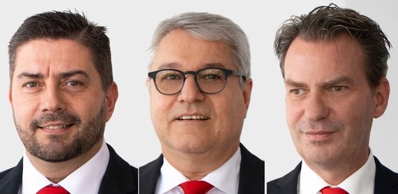 Drei Männer in Anzügen und Krawatten stehen nebeneinander.