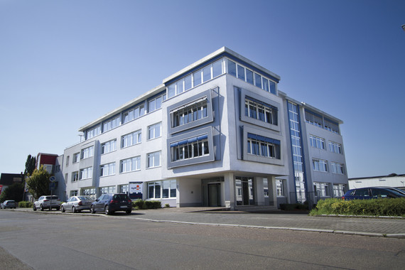 Ein modernes mehrstöckiges Bürogebäude mit großen Fenstern steht an einer Straße unter blauem Himmel.