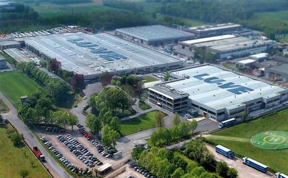 Luftaufnahme eines Industrie- und Bürokomplexes mit mehreren Gebäuden, Parkplätzen und umgebenden Bäumen.