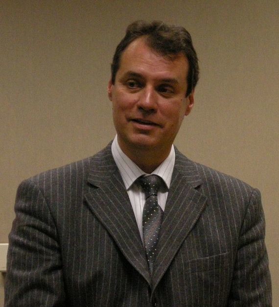 Ein Mann in einem gestreiften Anzug und Krawatte steht vor einem neutralen Hintergrund.