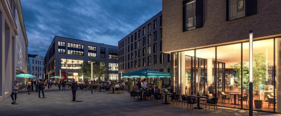 Ein beleuchtetes Restaurant mit großen Fenstern steht in einer städtischen Umgebung bei Dämmerung, während Menschen im Hintergrund spazieren.