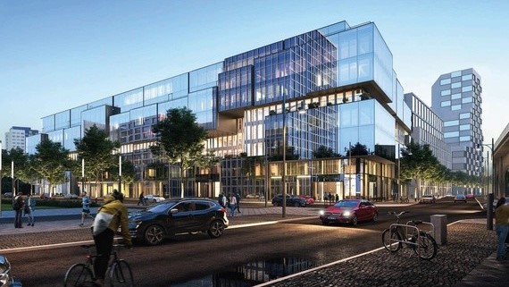 Ein modernes, gläsernes Bürogebäude mit beleuchteten Fenstern steht an einer belebten Straße bei Dämmerung.