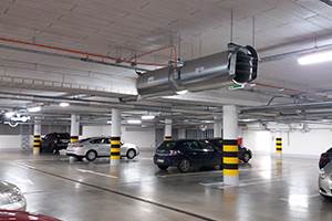 Ein beleuchtetes Parkhaus mit mehreren geparkten Autos und gelb-schwarzen Säulenmarkierungen.