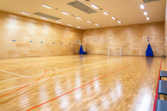 Leerer Sporthalle mit Holzboden, Basketballkorb und blauen Trainingsausrüstungen.