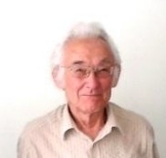 Ein älterer Mann mit grauem Haar und Brille trägt ein hellblaues Hemd mit einem gemusterten Muster.