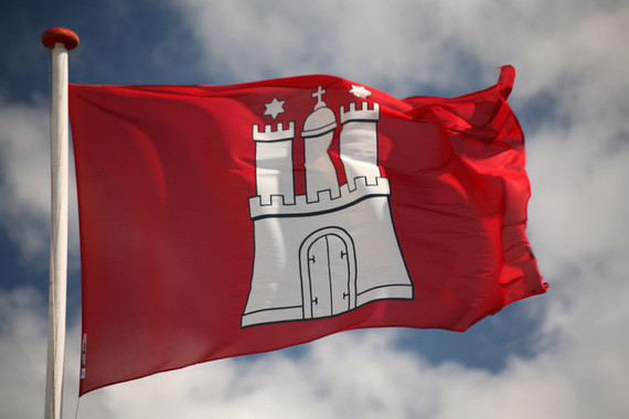 Eine rot-weiße Flagge mit dem Wappen von Hamburg weht im Wind vor einem bewölkten Himmel.