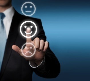 Ein Mann im Anzug berührt einen glücklichen Smiley auf einem Bildschirm, während traurige und neutrale Smileys daneben zu sehen sind.