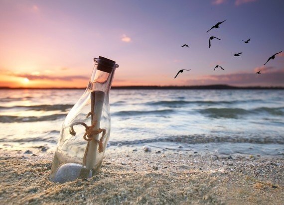 Eine Flaschenpost liegt am Strand bei Sonnenuntergang, während Vögel über dem Meer fliegen.