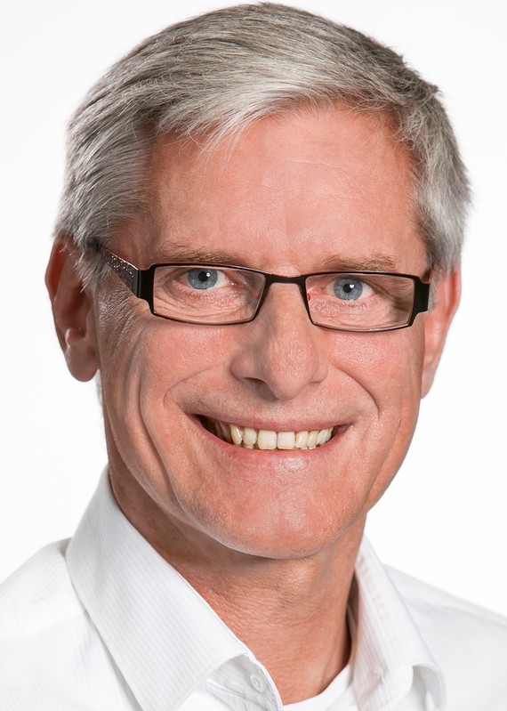 Ein Mann mit grauem Haar, Brille und einem weißen Hemd lächelt in die Kamera.