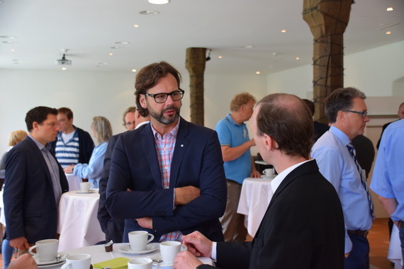 Mehrere Personen sitzen an Tischen in einem Veranstaltungssaal und unterhalten sich.