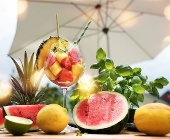 Ein fruchtiger Sommercocktail mit Ananas, Wassermelone und Zitronen auf einem Tisch unter einem Sonnenschirm.